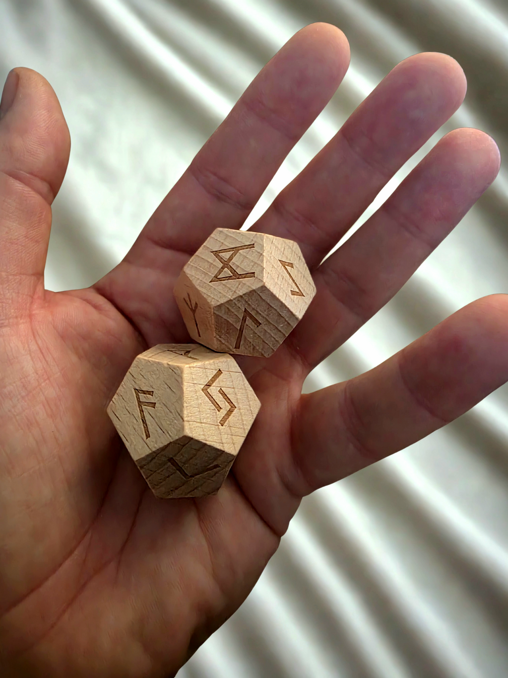Wooden dice with rune symbols held in a hand against a neutral background